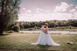 lesbisches brautpaar gender steht vor einem fluß bei gegenlicht und kuscheln sommerhochzeit